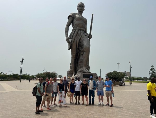 Group of people standing in front of a large statue holding a staff in an open public square