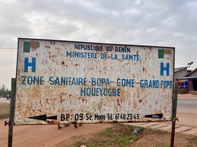 Weathered roadside sign reading “République du Bénin Ministère de la Santé” with location details for a health zone