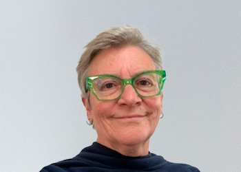 Photograph of Governor Helen Bown. Helen has short hair and white skin. She is wearing earings, stylish green glasses and a blue top.
