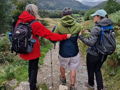 Sam walks along a rocky mountain path alongside two members of the Gloucestershire Brain Injury Team during the Helvellyn challenge.