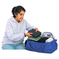 Person in a grey hoodie packing clothes into a blue duffel bag.