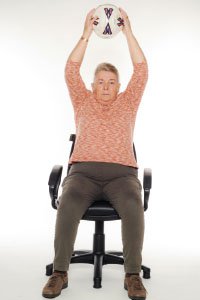 A woman doing seated exercises with a football raised above her head