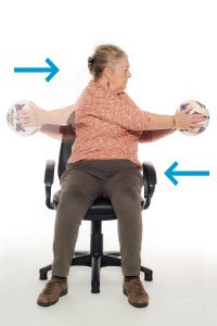 A woman doing seated exercises with a football, twisting left and right
