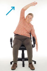 A woman doing chair exercises by doing overhead arm stretches