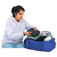 Person in a grey hoodie packing clothes into a blue duffel bag.