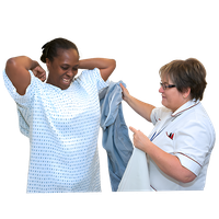 A nurse assists a smiling patient with her hospital gown.