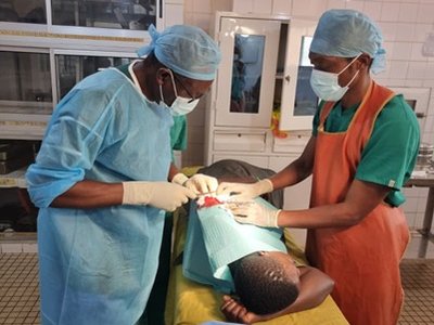 Two clinicians performing a procedure on a patient lying on a treatment table, with surgical instruments nearby